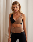 Nubyen Alicante V-Neck Wrap Sports Bra in Biscotti. The bra features a flattering wrap design, deep V-neckline, and smooth fabric for a stylish yet supportive fit. Styled with matching activewear, the look is showcased in a clean, modern setting with soft lighting to emphasize its neutral tone.