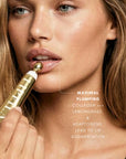 Woman applying a cosmetic product to her lips with text about maximal plumping collagen and lemongrass.