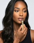 Woman applying gold lipstick to her lips against a plain background