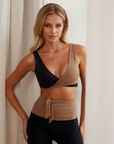 Nubyen Alicante V-Neck Wrap Sports Bra in Biscotti. The bra features a flattering wrap design, deep V-neckline, and smooth fabric for a stylish yet supportive fit. Styled with matching activewear, the look is showcased in a clean, modern setting with soft lighting to emphasize its neutral tone.