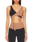 Nubyen Alicante V-Neck Wrap Sports Bra in Biscotti. The bra features a flattering wrap design, deep V-neckline, and smooth fabric for a stylish yet supportive fit. Styled with matching activewear, the look is showcased in a clean, modern setting with soft lighting to emphasize its neutral tone.