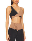 Nubyen Alicante V-Neck Wrap Sports Bra in Biscotti. The bra features a flattering wrap design, deep V-neckline, and smooth fabric for a stylish yet supportive fit. Styled with matching activewear, the look is showcased in a clean, modern setting with soft lighting to emphasize its neutral tone.