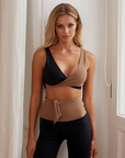 Nubyen Alicante V-Neck Wrap Sports Bra in Biscotti. The bra features a flattering wrap design, deep V-neckline, and smooth fabric for a stylish yet supportive fit. Styled with matching activewear, the look is showcased in a clean, modern setting with soft lighting to emphasize its neutral tone.