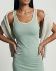 Sage green fitted athletic mini dress with soft cream contrast trim, body-contouring stretch fabric and minimalist sleeveless silhouette designed for elevated activewear, tennis-inspired styling and luxury everyday wear.