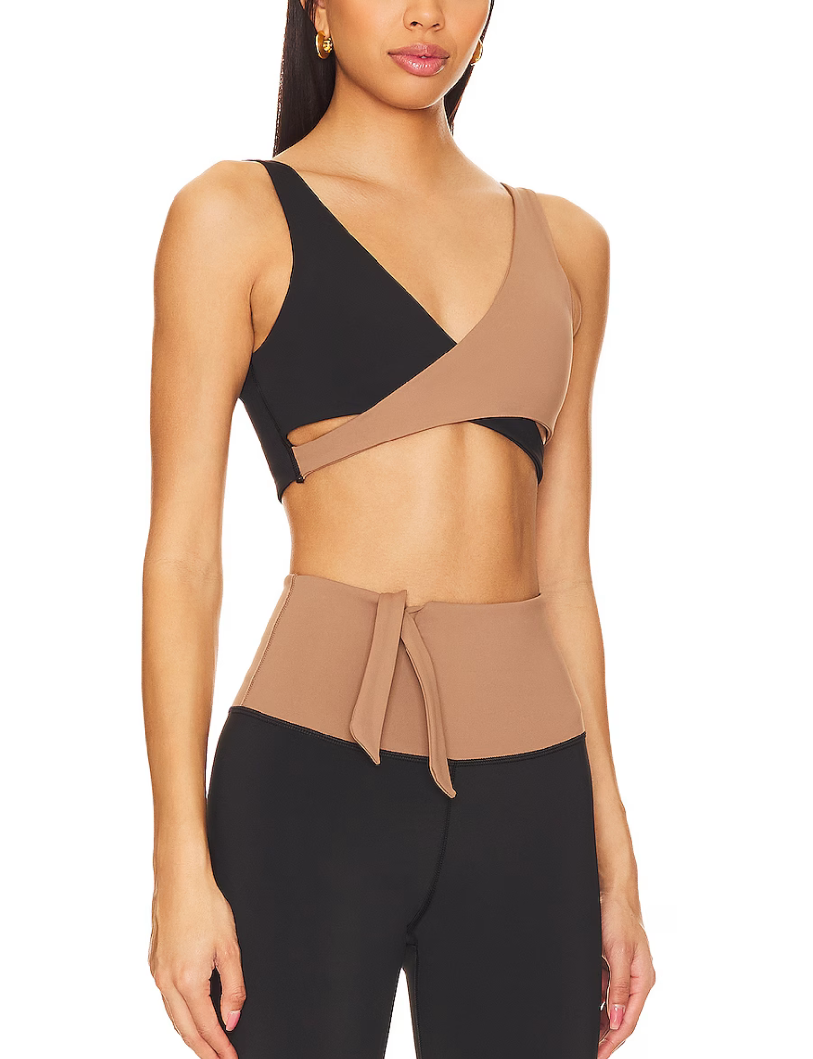 Nubyen Alicante V-Neck Wrap Sports Bra in Biscotti. The bra features a flattering wrap design, deep V-neckline, and smooth fabric for a stylish yet supportive fit. Styled with matching activewear, the look is showcased in a clean, modern setting with soft lighting to emphasize its neutral tone.