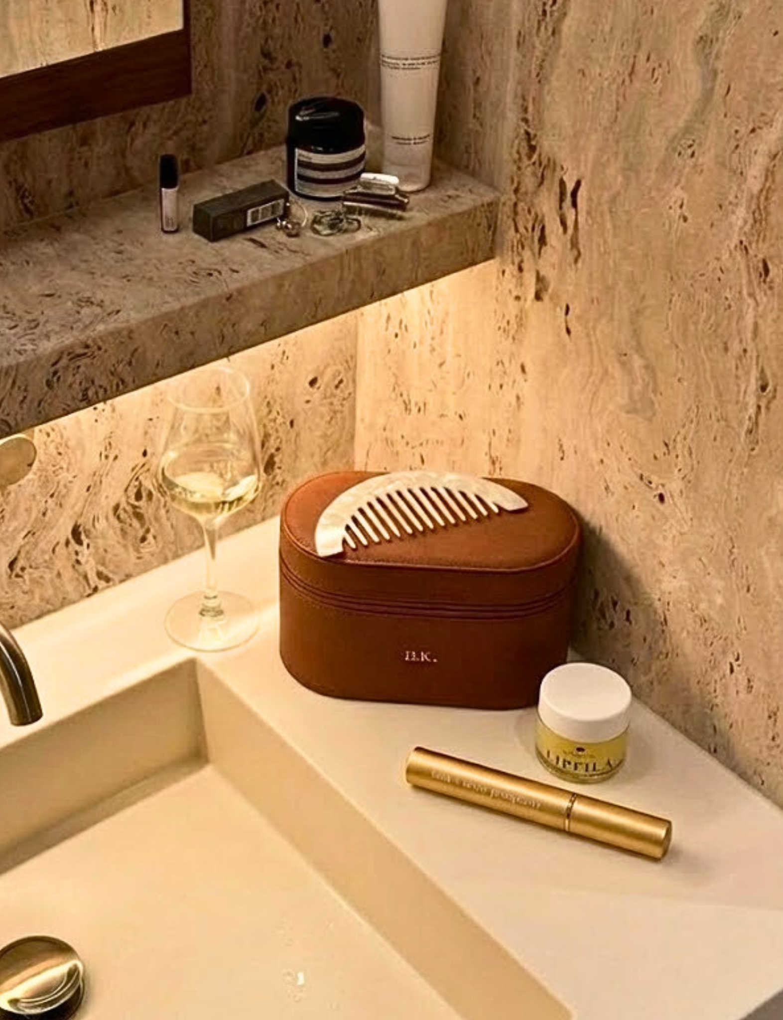Cosmetic case with a comb on a bathroom counter with various skincare products.